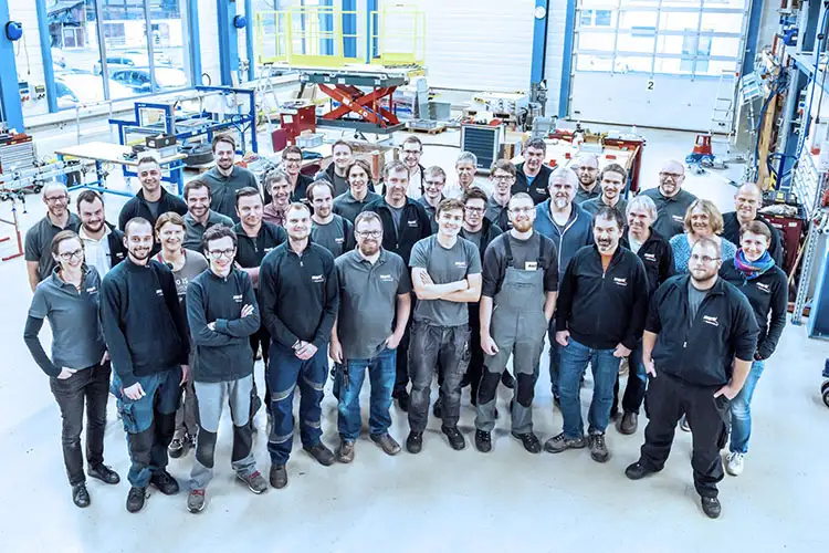 Eine Gruppe von Menschen steht in einer Fabrik und betrachtet die Maschinen und Arbeitsabläufe.